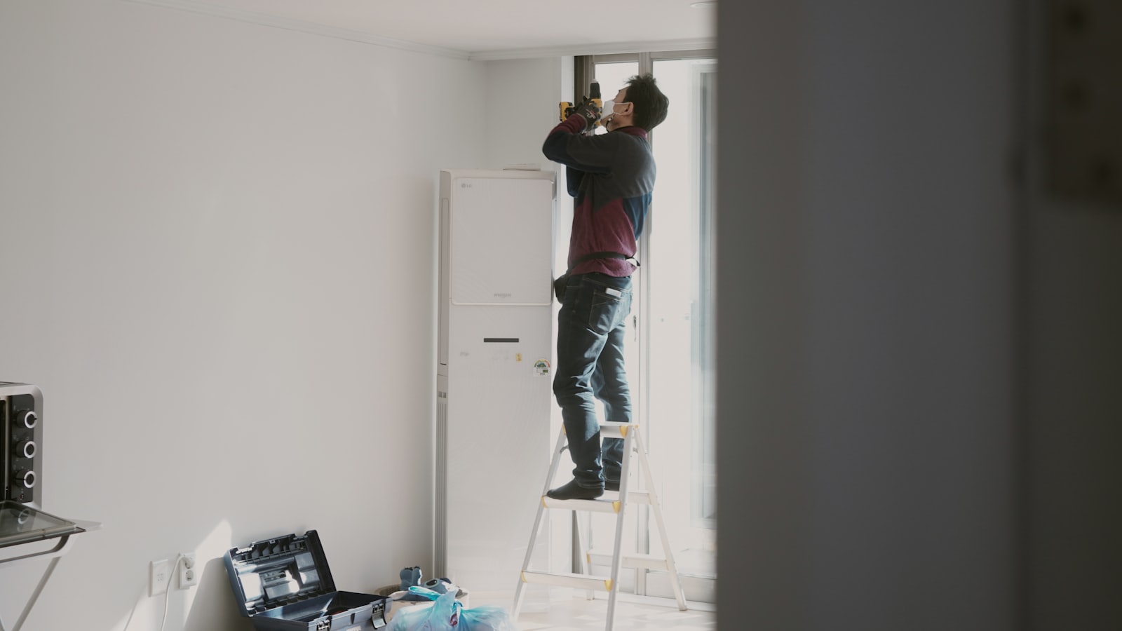 Handwerker montiert auf einer Leiter stehend etwas an der Wand einer fertigen Wohnung